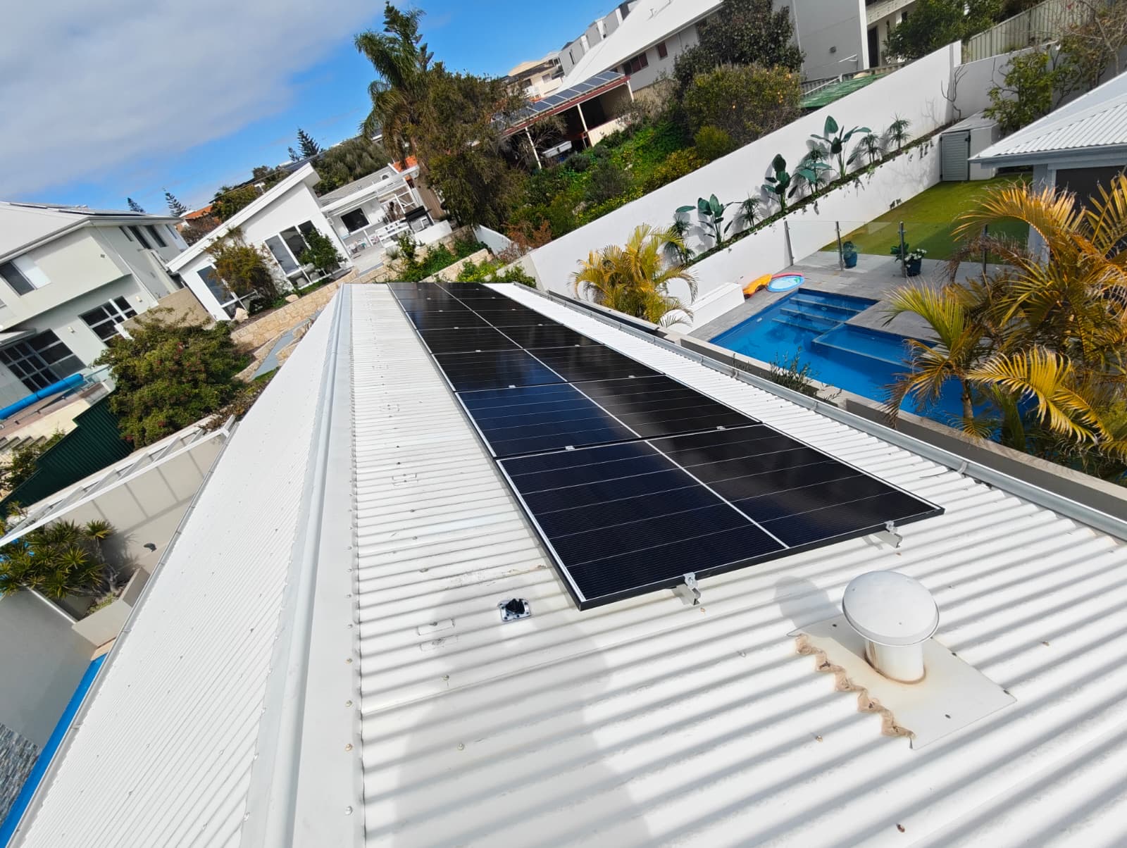 Jinko solar panels on a flat metal roof section beside a Perth backyard pool